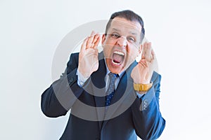 Middle age man shouting crazy with hands over mouth over white wall background