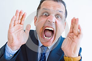 Middle age man shouting crazy with hands over mouth over white wall background