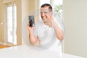 Middle age man showing smartphone screen happy with big smile doing ok sign, thumb up with fingers, excellent sign