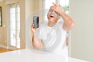 Middle age man showing smartphone screen stressed with hand on head, shocked with shame and surprise face, angry and frustrated