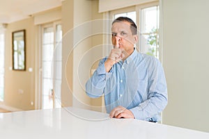 Middle age man sitting at home asking to be quiet with finger on lips