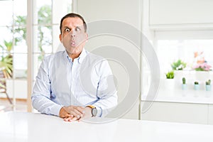 Middle age man sitting at home making fish face with lips, crazy and comical gesture
