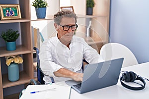 Middle age man sitting on wheelchair teleworking at home