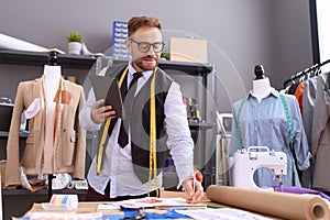 Middle age man tailor using touchpad writing on notebook at atelier