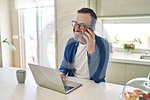 Middle age man talking on the smartphone and using laptop at home