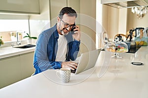 Middle age man talking on the smartphone and using laptop at home