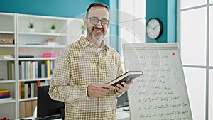 Middle age man teacher teaching lesson holding book at classroom