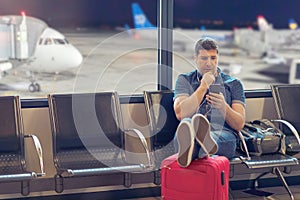 Middle age man tourist using smart phone in airport terminal looking at flight delayed schedules