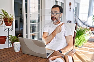 Middle age man using computer laptop at home pointing aside worried and nervous with forefinger, concerned and surprised