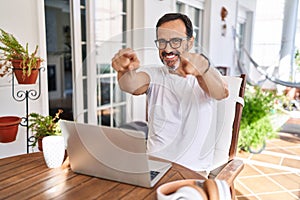 Middle age man using computer laptop at home pointing to you and the camera with fingers, smiling positive and cheerful