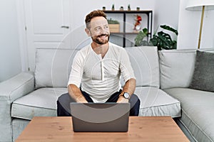 Middle age man using laptop at home looking away to side with smile on face, natural expression