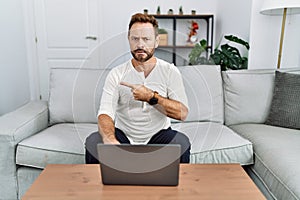 Middle age man using laptop at home pointing aside worried and nervous with forefinger, concerned and surprised expression