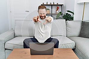 Middle age man using laptop at home pointing to you and the camera with fingers, smiling positive and cheerful