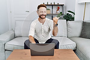 Middle age man using laptop at home smiling with happy face looking and pointing to the side with thumb up