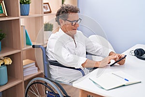 Middle age man using smartphone sitting on wheelchair teleworking at home