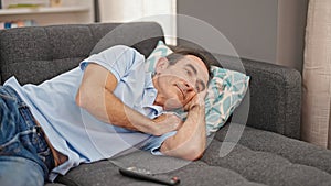 Middle age man watching tv lying on sofa with boring expression at home