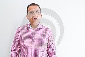 Middle age man wearing business shirt over white wall afraid and shocked with surprise expression, fear and excited face