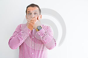 Middle age man wearing business shirt over white wall shocked covering mouth with hands for mistake