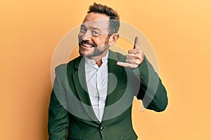 Middle age man wearing business suit smiling doing phone gesture with hand and fingers like talking on the telephone