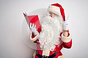 Middle age man wearing Santa Claus costume reading book over isolated white background smiling looking to the camera showing