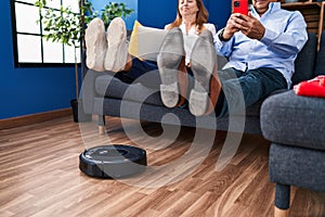 Middle age man and woman couple cleaning floor using robot cleaner at home