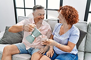 Middle age man and woman couple drinking coffee sitting on sofa at home