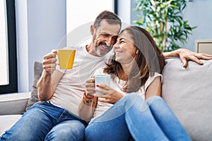 Middle age man and woman couple drinking coffee sitting on sofa at home