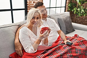 Middle age man and woman couple drinking coffee and watching tv at home