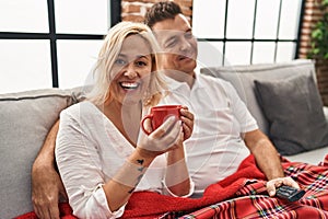 Middle age man and woman couple drinking coffee and watching tv at home