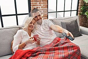 Middle age man and woman couple drinking coffee and watching tv at home