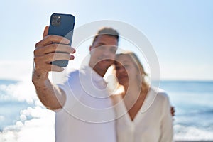 Middle age man and woman couple hugging each other make selfie by the smartphone at seaside