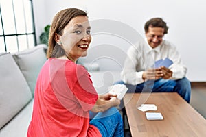 Middle age man and woman couple smiling confident playing poker cards at home