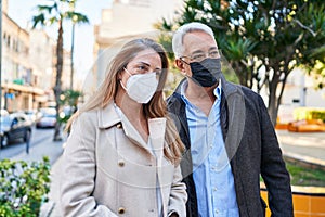 Middle age man and woman couple wearing medical mask standing at park