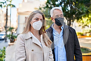 Middle age man and woman couple wearing medical mask standing at park