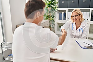 Middle age man and woman doctor and patient shake hands having medical consultation at clinic