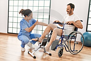 Middle age man and woman having rehab session pedaling sitting on wheelchair at physiotherapy clinic