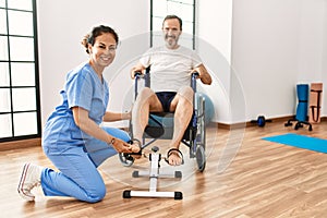 Middle age man and woman having rehab session pedaling sitting on wheelchair at physiotherapy clinic