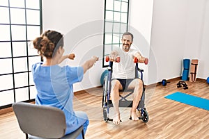 Middle age man and woman having rehab session using dumbbells sitting on wheelchair at physiotherapy clinic