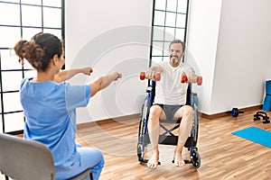 Middle age man and woman having rehab session using dumbbells sitting on wheelchair at physiotherapy clinic