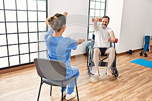 Middle age man and woman having rehab session using dumbbells sitting on wheelchair at physiotherapy clinic
