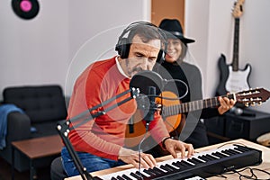 Middle age man and woman musicians playing guitar and keyboard piano singing song at music studio