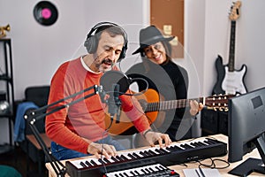 Middle age man and woman musicians playing guitar and keyboard piano singing song at music studio