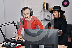 Middle age man and woman musicians playing guitar and keyboard piano singing song at music studio