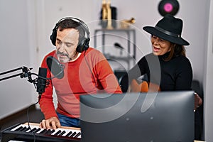 Middle age man and woman musicians playing guitar and keyboard piano singing song at music studio