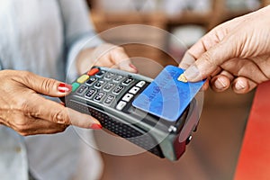 Middle age man and woman paying using credit card and data phone at clothing store