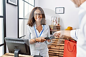 Middle age man and woman smiling confident paying using credit card and data phone at clothing store