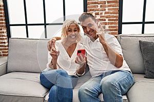 Middle age man and woman using smartphone sitting on the sofa surprised with an idea or question pointing finger with happy face,