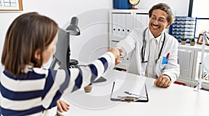 Middle age man and woman wearing doctor uniform having medical consultation shake hands at clinic