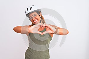 Middle age mature cyclist woman wearing safety helmet over isolated background smiling in love doing heart symbol shape with hands