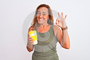 Middle age mature woman drinking a take away cup of coffee over isolated background doing ok sign with fingers, excellent symbol